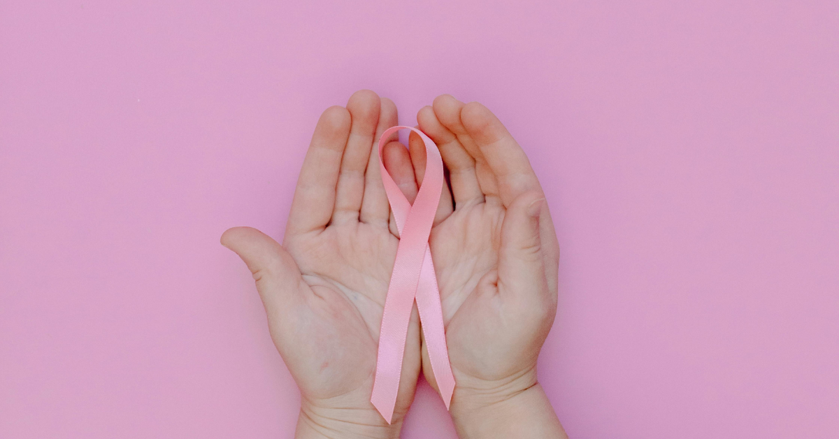 Dos manos sosteniendo un lazo rosado en relación al cancer de mama.