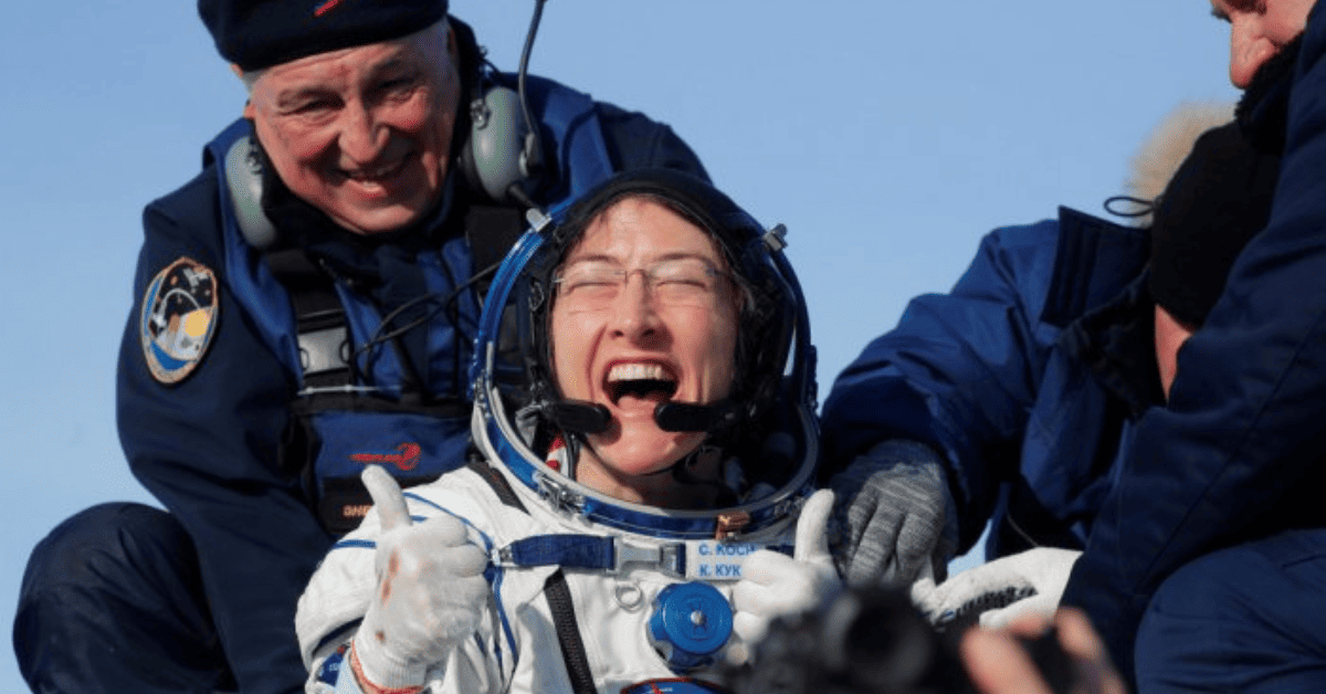 Christina Koch sonriente y con el pulgar arriba, junto a dos hombres ayudándola a bajar de la nave.
